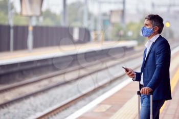 Businessman On Railway Platform With Mobile Phone Wearing PPE Face Mask During Health Pandemic