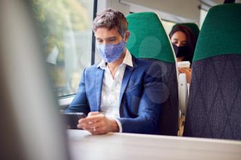 Businessman On Train Streaming To Mobile Phone Wearing PPE Face Mask During Health Pandemic