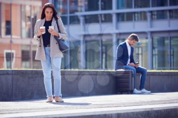 Businesswoman With Takeaway Coffee Walking To Office Looking At Mobile Phone