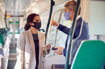 Business Commuters Stand In Train Carriage With Mobile Phones Wearing PPE Face Masks During Pandemic