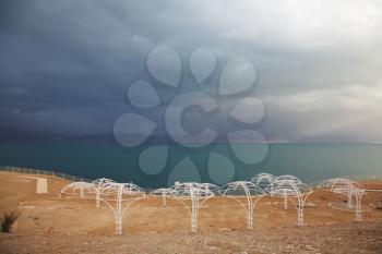 Winter on the Dead Sea. Empty beach umbrellas, green water and purple thunderheads