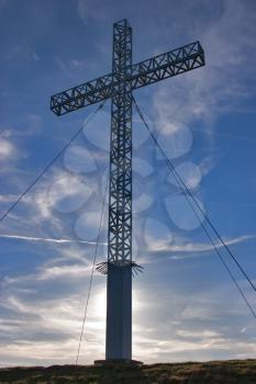  A metal tower in the form of a cross at top of mountain, strengthened by cables