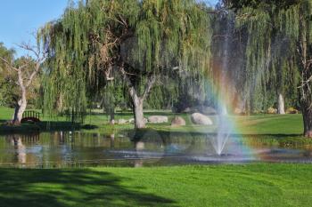 Decorative fountain, trees and shining rainbow on the golf course