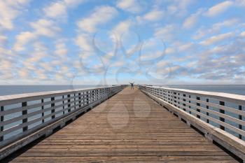 Wooden pier with a handrail. Pacific coast of California, the USA. The lonely tourist at pier edge
