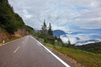 Wet shiny road in the Swiss Alps. Cold autumn day, low cumulus clouds
