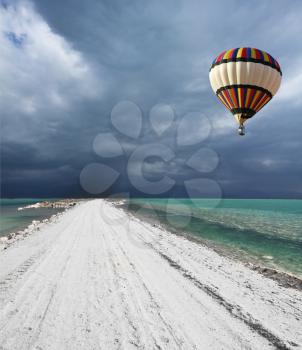 Picturesque bright balloon with a basket of passenger flying in a thunderstorm over the Dead Sea
