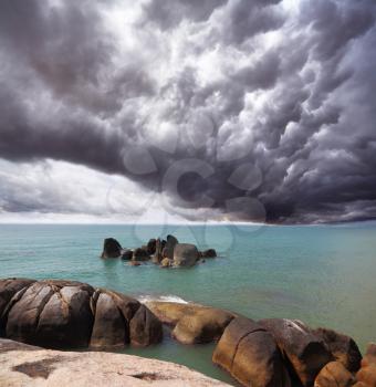 Storm cloud over the southern sea. Coastal rocks shine under the sunset sun