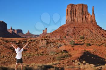 The enthusiastic tourist in a white shirt in Monument Valley. The famous monolith of red sandstone - Mittens.