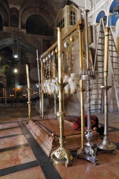 The pilgrim in red clothes passionately prays under icon lamps. Temple of the Holy Sepulcher in Jerusalem. The oldest Christian sanctuary - Stone of Unction.