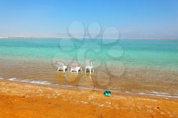 White beach armchairs, chair and green slippers in the warm clear water beach. Beach on the Dead Sea, a sunny day in May