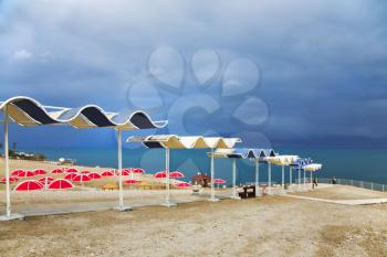 Red beach umbrellas on empty deserted deserted coast of the Dead Sea in a thunder-storm 