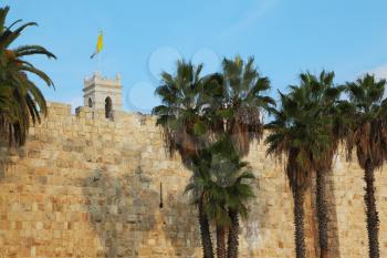 Walls of Jerusalem ancient. Palm trees and flags
