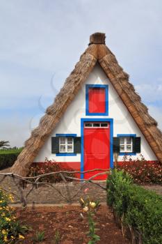 Pastoral landscape. Small rural house with a triangular thatched roof. The red door and small windows with shutters. Madeira, the city of Santana