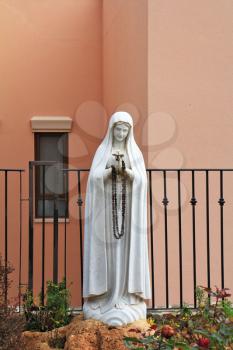 The sculptural image of Maiden Maria with beads in hands. A white sculpture.
