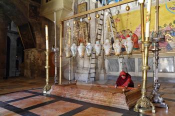 The pilgrim in red clothes passionately prays under icon lamps.  Temple of the Holy Sepulcher in Jerusalem. The oldest Christian sanctuary - Stone of Unction. 