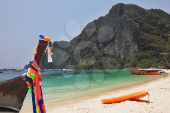 Ancient boat Longtail decorated with multi-colored silk ribbons and modern red sports canoes. Island Phi-Phi, Thailand
