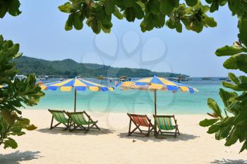 Tropical paradise on the bank of the azure sea. Multi-colored beach umbrellas and chaise lounges on white sand
