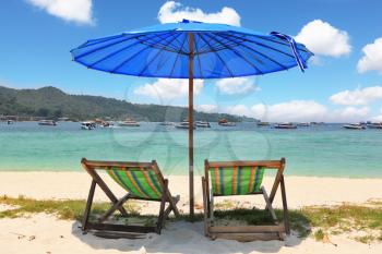 A picturesque dark blue beach umbrella and striped chaise lounges on white beach sand
