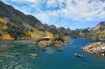 Fishing paradise. Azure lake in autumn mountains. Fishing boats turn round small picturesque island