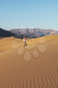 A magnificent sunrise amongst the sand dunes. Woman photographer in a straw hat photographing sand waves
