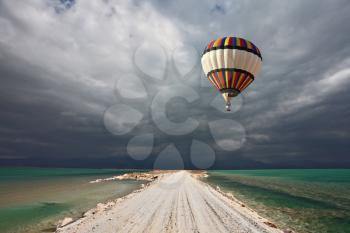 Picturesque bright balloon with a basket of passenger flying in a thunderstorm over the shoal Dead Sea
