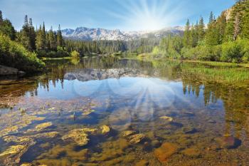 The magnificent mountains and northern sun are reflected in the smooth waters of a mountain lake