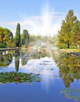  Magnificent Italian park at sunset. Smooth water of a pond reflects coastal cypresses and picturesque bushes