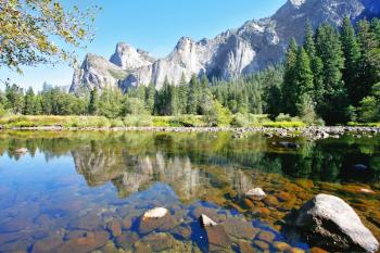 The magnificent Yosemite Valley. Three scenic rocky peaks and blue sky reflected in the smooth waters of the Merced