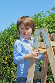 The beautiful green-eyed boy spoiled by attention climbed up a wooden sliding ladder and doesn't want to go down