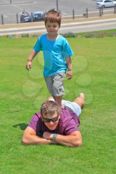 Adorable four year old boy having fun playing with his uncle on a green grass lawn