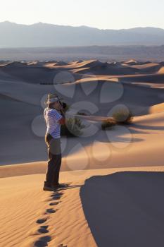 A magnificent sunrise amongst the sand dunes. Woman photographer in a striped T-short photographing sand waves