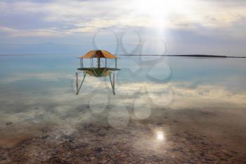 Medical beach on the Dead Sea, Israel. Round gazebo in the water near the water's edge. Cloudy sky reflected in water