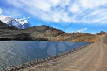 Gravel road along the shore of the lake with the cold blue water. Patagonia, Chile