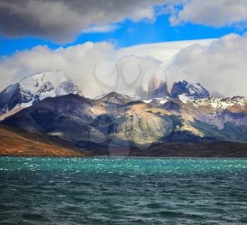 Fantastic beauty of the national park Torres del Paine in Chilean Patagonia. Strong wind drives wave in Laguna Azul emerald water. On the horizon are seen the famous cliffs of Torres