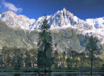 Chamonix - a famous ski resort in the French Alps. Reflections of snow-capped peaks and coastal trees in city park pond
