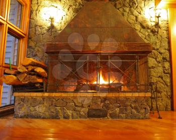 Huge burning fireplace. Lobby of magnificent hotel, a parquet floor and the stone wall shined with wall lamps