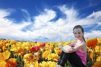 Charming beautiful six year old girl sitting and smiling in a field of blossoming yellow and red buttercups