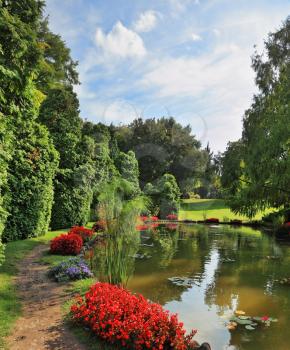 A quiet corner of the picturesque park in Europe. A pond, overgrown with lilies  and red flower beds