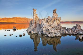 The magic of Mono Lake. Outliers - bizarre limestone calcareous tufa formation reflected in the smooth water. Orange sunset