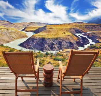 Two wooden chairs - on a wooden platform.  The comfortable place to enjoy the beauty of the landscape. The magnificent national park Torres del Paine in Chile. 
Picturesque river bends a horseshoe of 
