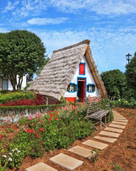 Traditional rural landscape. The little white house with a triangular thatched roof and a red door. The village - Museum of the Portuguese island of Madeira