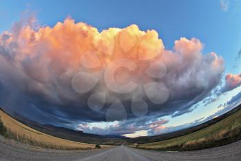 Huge pink - orange cloud, like a bowl of cream, lit the last rays of sunset. Gravel road through the Patagonian steppe. Picture taken Fisheye lens