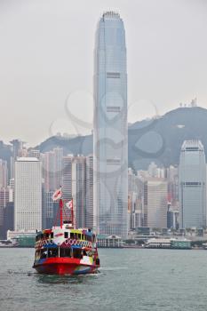 Brightly painted tourist boat in the sea ​​strait of Hong Kong. On the waterfront in the mist modern skyscrapers