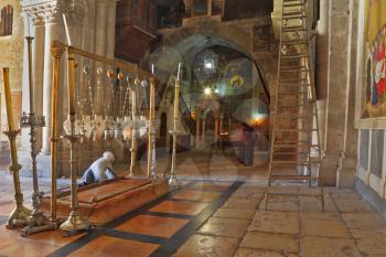 Temple of the Holy Sepulcher in Jerusalem. The oldest Christian sanctuary - Stone of Unction. The pilgrim in white clothes prays under icon lamps.
