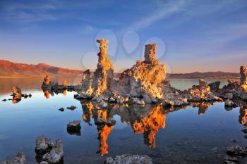The magic of Mono Lake. Outliers - bizarre calcareous tufa formation on the smooth water of the lake. Orange sunset