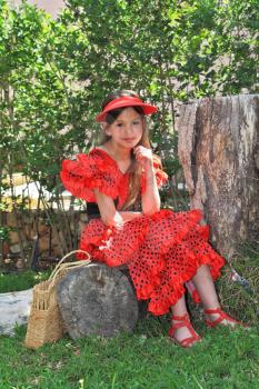 The charming eight-year girl on walk in park. The girl is dressed in a red dress of the dancer of a flamenco.