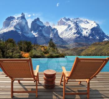 The magnificent national park Torres del Paine in Chile. Snow-covered cliffs of Los Kuernos rise on the shores of Lake Pehoe. Two wooden chairs mounted on a wooden platform.  The comfortable place to 