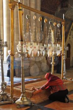 Temple of the Holy Sepulcher in Jerusalem. The oldest Christian sanctuary - Stone of Unction. The pilgrim in red clothes passionately prays under icon lamps.