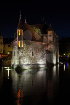 Summer night in the charming medieval town. Old fortress-prison on the island in the middle of the river. Castle illuminated by spotlights and is beautifully reflected in the dark water.