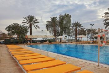 Winter in the Dead Sea. The picturesque swimming pool, palm trees and yellow beach loungers